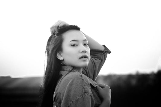 Black and white portrait of a woman outdoors wearing a denim jacket, looking at the camera.