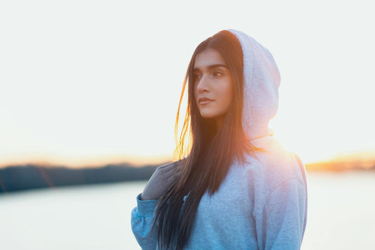 A young woman in a gray hoodie gazes thoughtfully towards the sunset, creating a serene outdoor portrait.